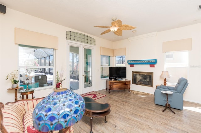 living room featuring a ceiling fan, a glass covered fireplace, and wood finished floors