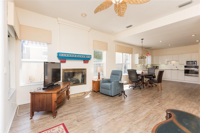 living area with light wood finished floors, visible vents, and a glass covered fireplace