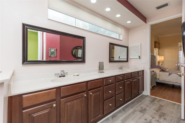 ensuite bathroom with double vanity, wood finished floors, visible vents, and a sink