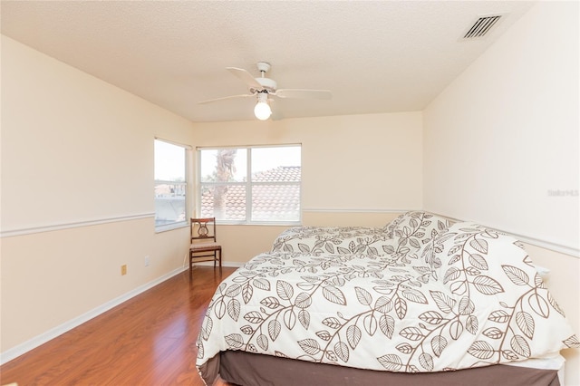 bedroom featuring visible vents, baseboards, wood finished floors, a textured ceiling, and a ceiling fan