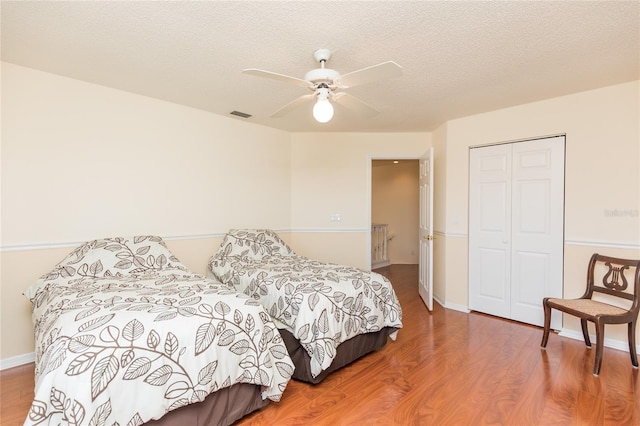 bedroom with a ceiling fan, wood finished floors, visible vents, a closet, and a textured ceiling