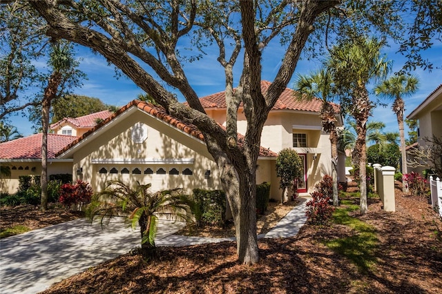 mediterranean / spanish-style home featuring a garage, a tile roof, concrete driveway, and stucco siding