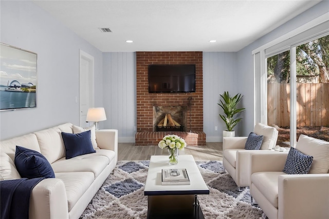 living area with visible vents, a brick fireplace, baseboards, and wood finished floors