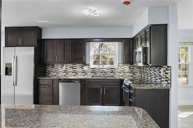 kitchen with dark stone countertops, a healthy amount of sunlight, appliances with stainless steel finishes, and a sink