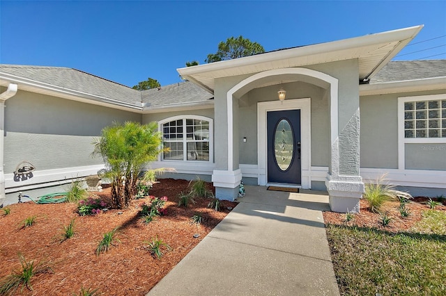 entrance to property with a shingled roof and stucco siding