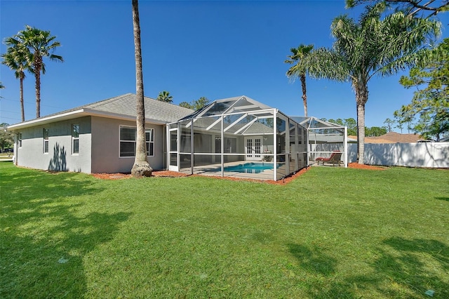 rear view of house with stucco siding, a lawn, fence, glass enclosure, and a fenced in pool