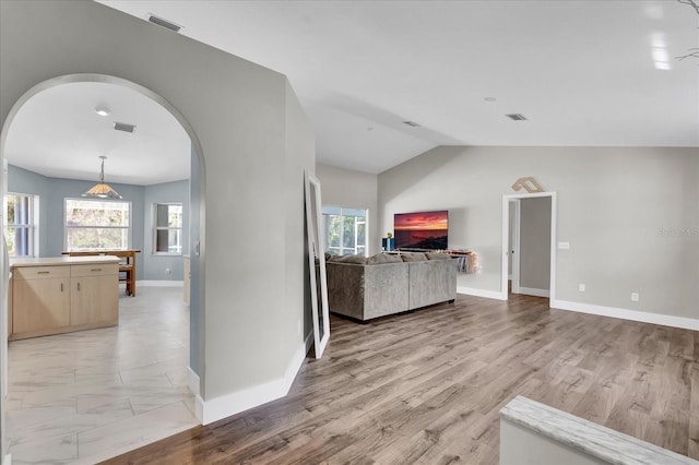 unfurnished living room featuring visible vents, arched walkways, plenty of natural light, and vaulted ceiling