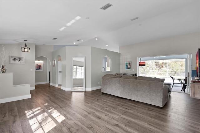 unfurnished living room featuring plenty of natural light, wood finished floors, and arched walkways