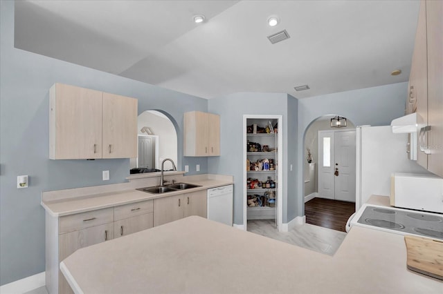 kitchen with a sink, white appliances, arched walkways, and light brown cabinets