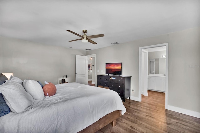 bedroom featuring wood finished floors, visible vents, baseboards, ensuite bath, and ceiling fan