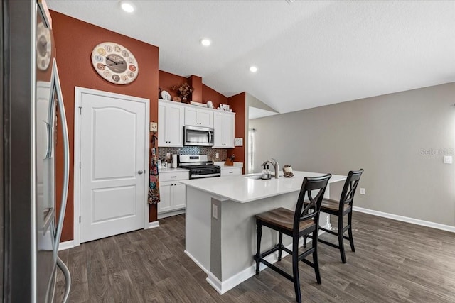 kitchen with tasteful backsplash, dark wood finished floors, appliances with stainless steel finishes, a breakfast bar area, and vaulted ceiling