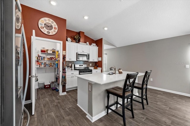 kitchen featuring dark wood-type flooring, a breakfast bar area, lofted ceiling, decorative backsplash, and appliances with stainless steel finishes