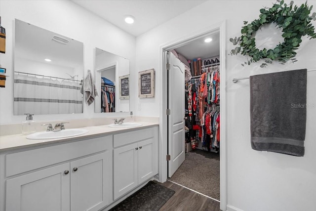 full bathroom with a sink, a walk in closet, wood finished floors, and double vanity