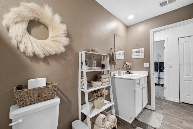 bathroom featuring visible vents, toilet, wood finished floors, baseboards, and vanity