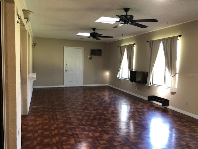 spare room with baseboards, ceiling fan, a wall unit AC, a skylight, and a textured ceiling