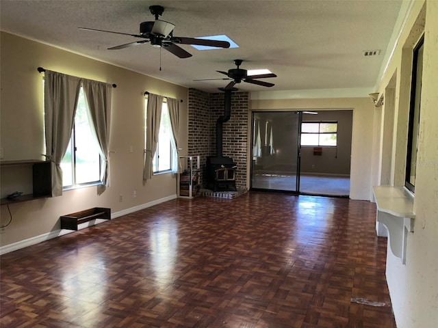 unfurnished living room featuring a wood stove, a healthy amount of sunlight, baseboards, and a textured ceiling