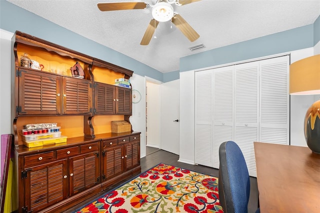 office space with visible vents, a textured ceiling, dark wood-style floors, and a ceiling fan