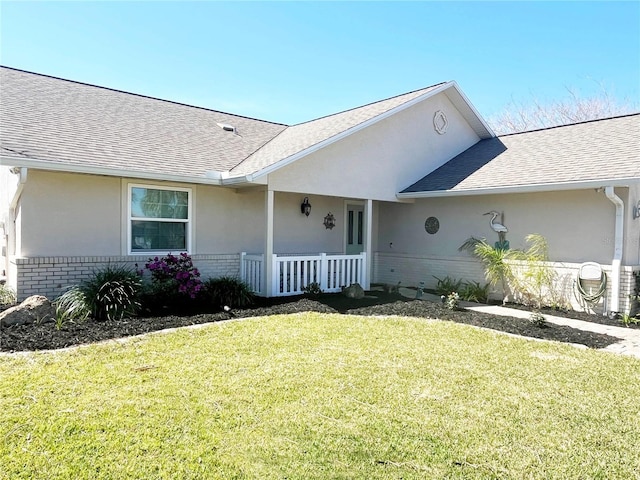 view of front facade featuring brick siding, stucco siding, a front yard, and roof with shingles