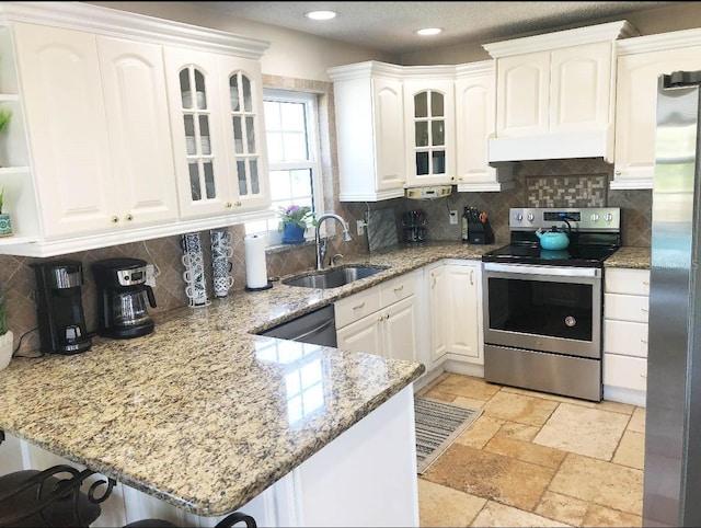 kitchen featuring a peninsula, a sink, stone tile flooring, stainless steel appliances, and white cabinetry