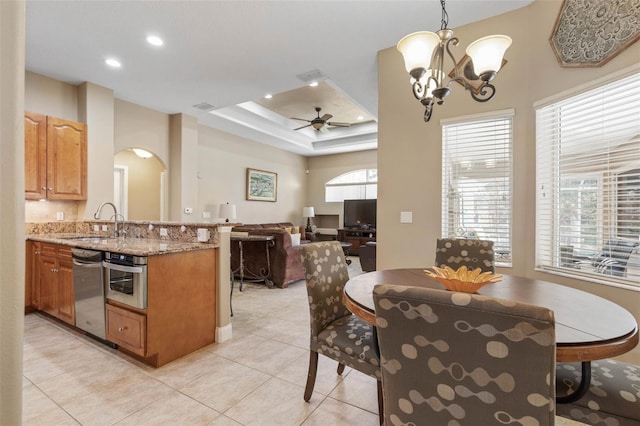 kitchen with ceiling fan with notable chandelier, a sink, arched walkways, appliances with stainless steel finishes, and a raised ceiling