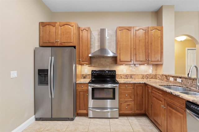 kitchen featuring light stone counters, appliances with stainless steel finishes, arched walkways, wall chimney exhaust hood, and a sink