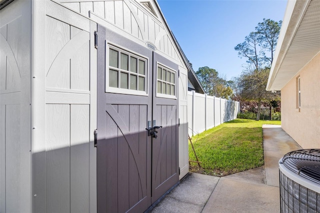 view of property exterior with a storage unit, central air condition unit, a lawn, fence, and an outdoor structure