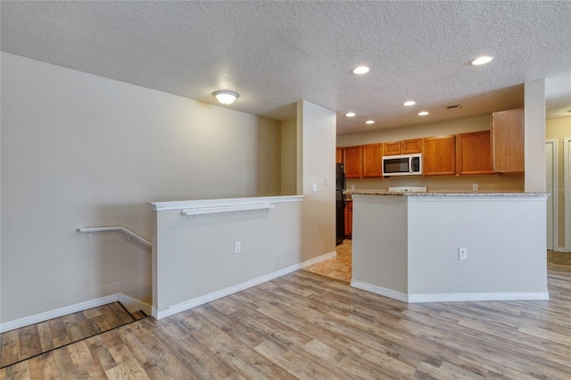 kitchen with light wood-style flooring, stainless steel microwave, freestanding refrigerator, recessed lighting, and baseboards