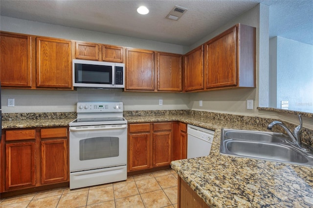 kitchen with visible vents, a sink, a textured ceiling, white appliances, and light tile patterned floors