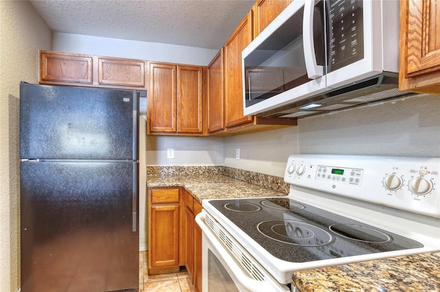 kitchen with brown cabinetry, light tile patterned floors, white appliances, and a textured ceiling