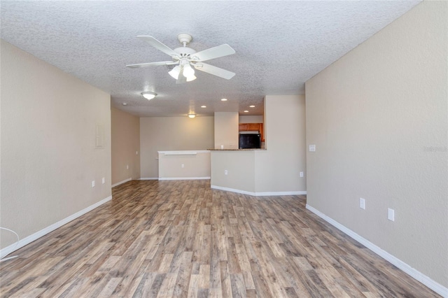 unfurnished living room with ceiling fan, baseboards, a textured ceiling, and light wood-style flooring