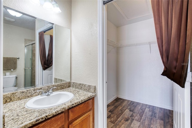 bathroom with a walk in closet, toilet, a stall shower, wood finished floors, and vanity