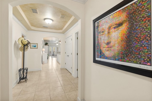 hallway with visible vents, arched walkways, a raised ceiling, and light tile patterned flooring