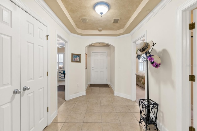 hall featuring light tile patterned floors, visible vents, arched walkways, and a raised ceiling