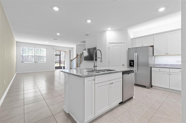 kitchen featuring light stone countertops, open floor plan, appliances with stainless steel finishes, white cabinetry, and a sink