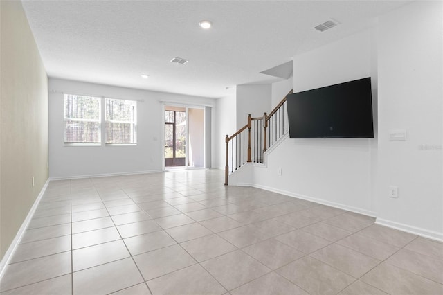 unfurnished living room featuring visible vents, a textured ceiling, light tile patterned flooring, and stairway