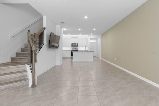 unfurnished living room featuring baseboards, stairway, light tile patterned floors, recessed lighting, and a sink