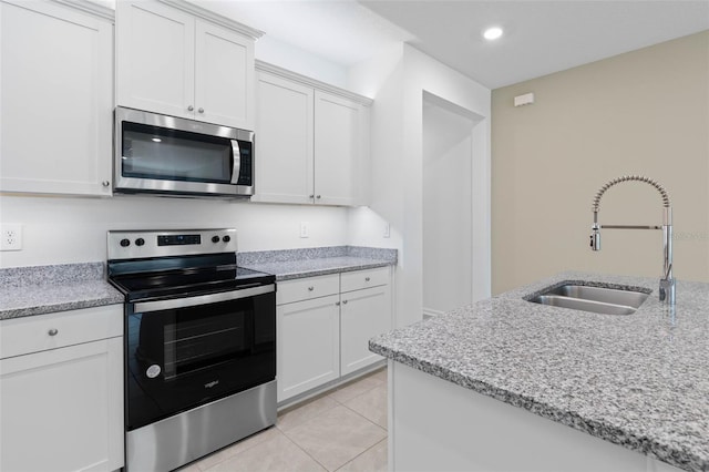 kitchen with light stone counters, light tile patterned floors, a sink, stainless steel appliances, and white cabinetry