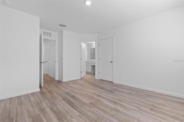 unfurnished bedroom featuring light wood-type flooring, visible vents, baseboards, and ensuite bathroom