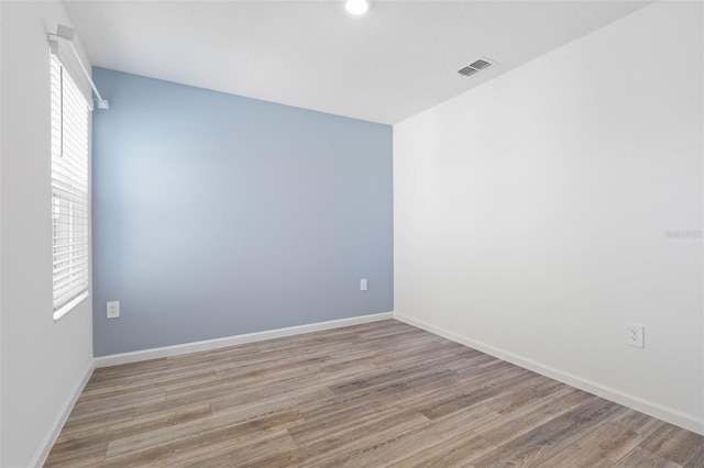 spare room featuring wood finished floors, visible vents, and baseboards