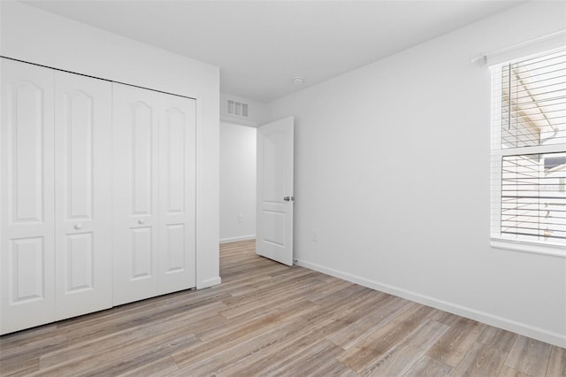 unfurnished bedroom featuring a closet, visible vents, light wood-style flooring, and baseboards