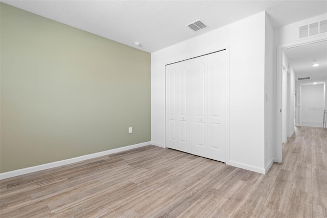 unfurnished bedroom featuring a closet, baseboards, visible vents, and light wood finished floors