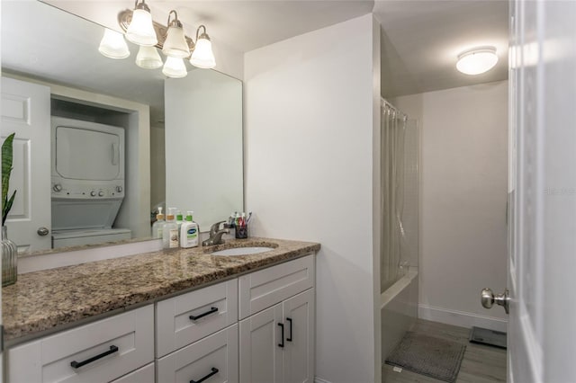 full bath with stacked washer and dryer, shower / bath combo, an inviting chandelier, baseboards, and vanity