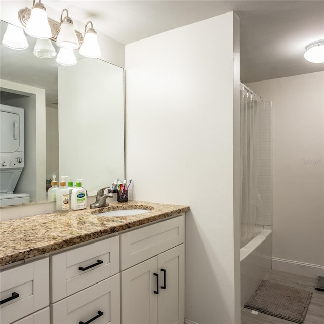 full bath with baseboards, stacked washer and dryer, shower / tub combo, an inviting chandelier, and vanity