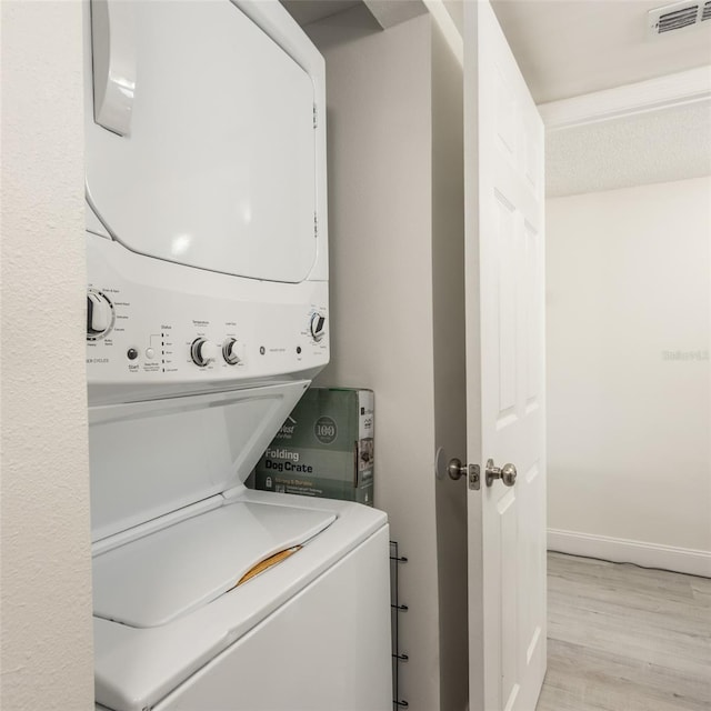 laundry room featuring visible vents, baseboards, laundry area, light wood-style flooring, and stacked washing maching and dryer