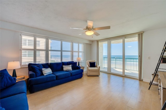 living room with a wall of windows, baseboards, ceiling fan, a water view, and light wood-type flooring