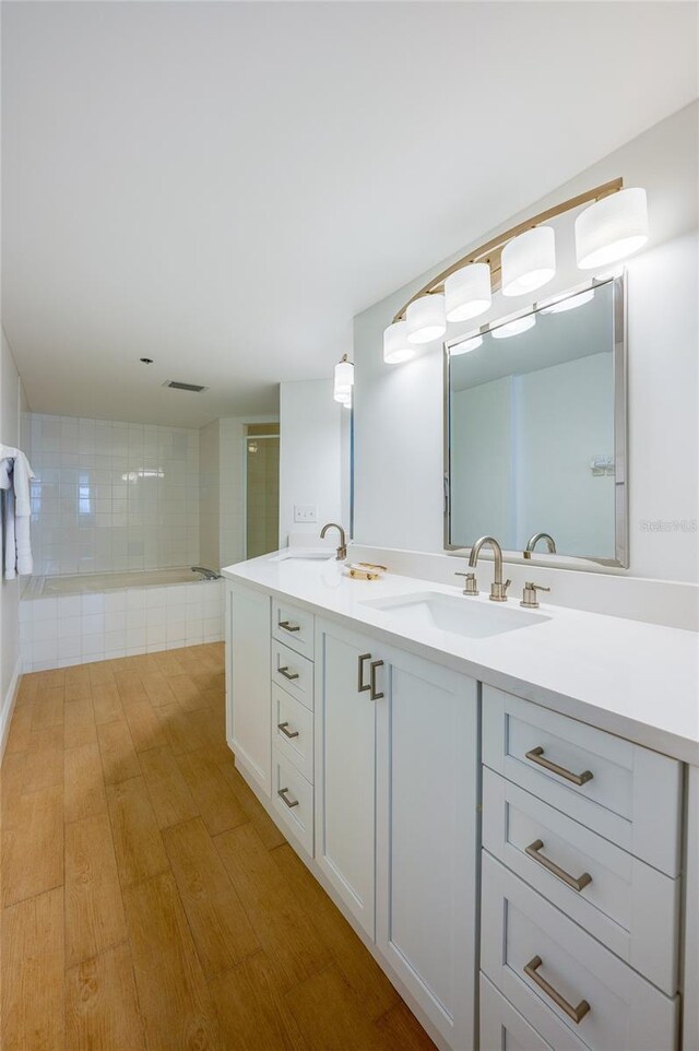 bathroom featuring wood finished floors, tiled shower, double vanity, and a sink