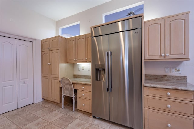 kitchen with light tile patterned floors, light stone countertops, light brown cabinets, built in study area, and high end refrigerator