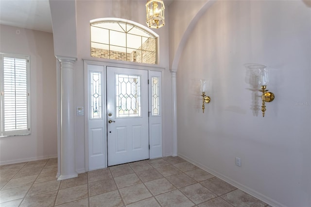 entryway featuring light tile patterned floors, baseboards, a notable chandelier, and ornate columns