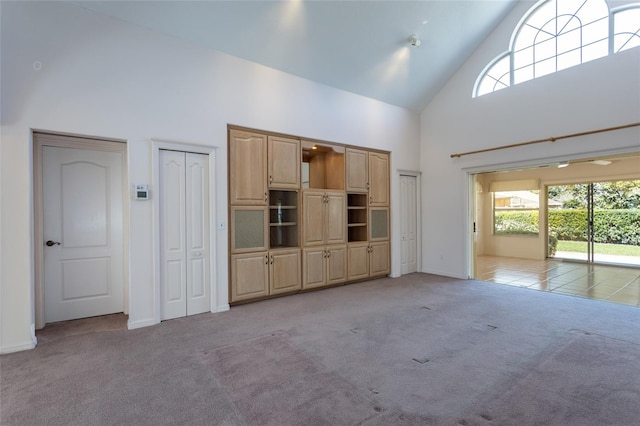 unfurnished living room featuring baseboards, light colored carpet, and high vaulted ceiling