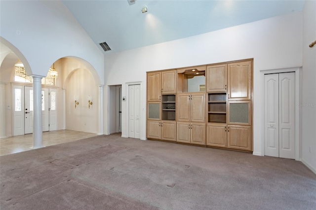 unfurnished living room featuring visible vents, light colored carpet, arched walkways, high vaulted ceiling, and ornate columns